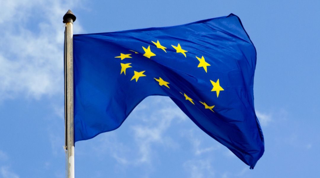 Symbolbild: Die europäische Flagge weht im Wind, dahinter ist hellblauer Himmel.